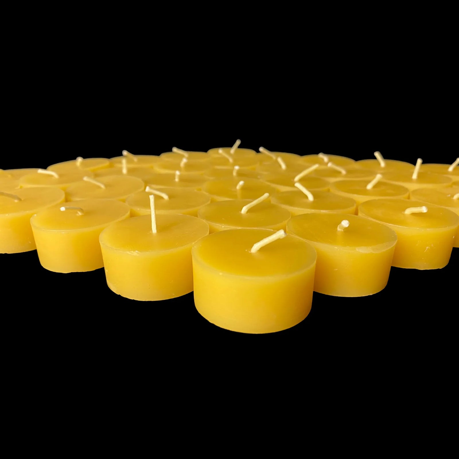 Yellow beeswax tea lights fanned across black in bulk, hand poured refills