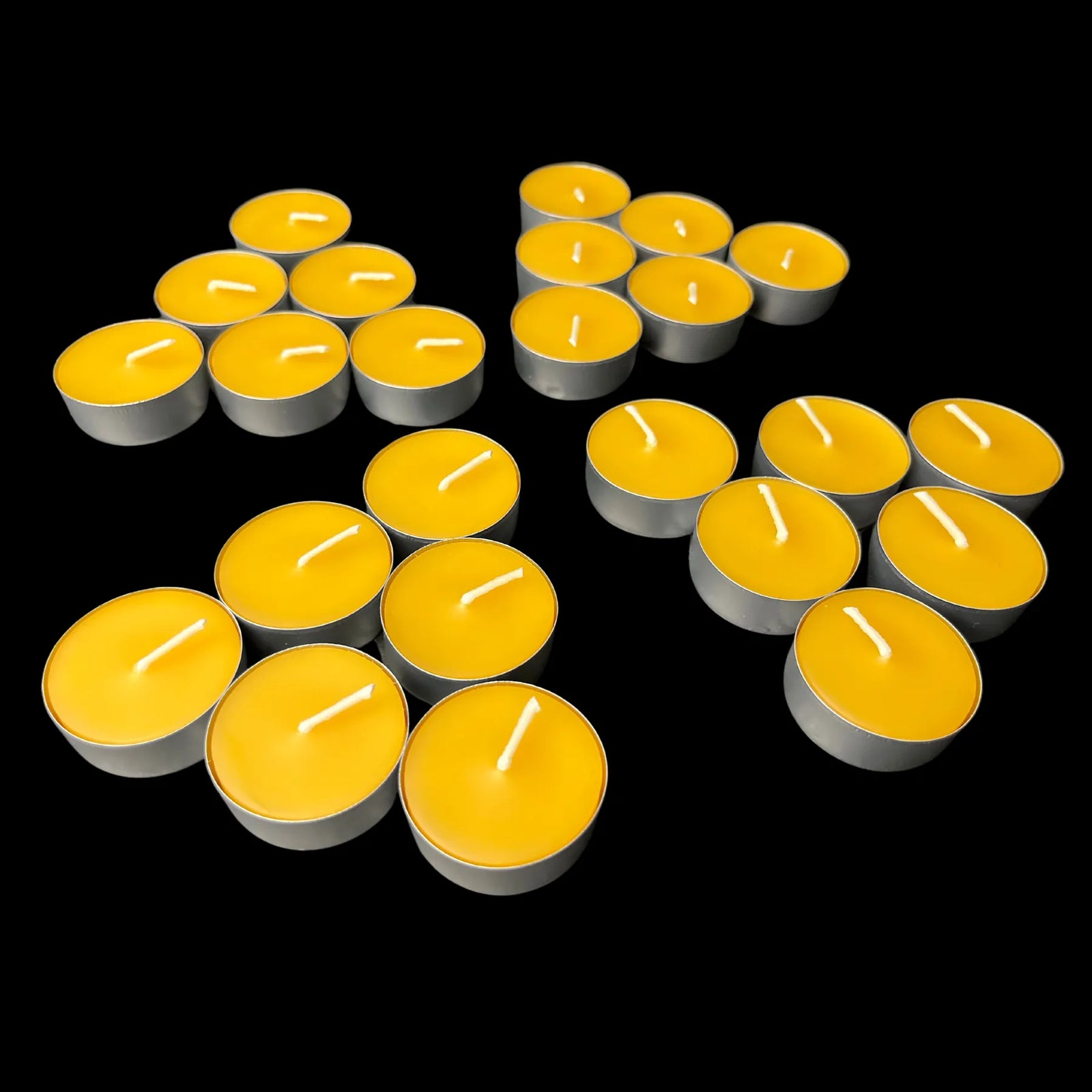 Honey-gold yellow beeswax tea lights in aluminum cups in a loose scatter, 100% beeswax
