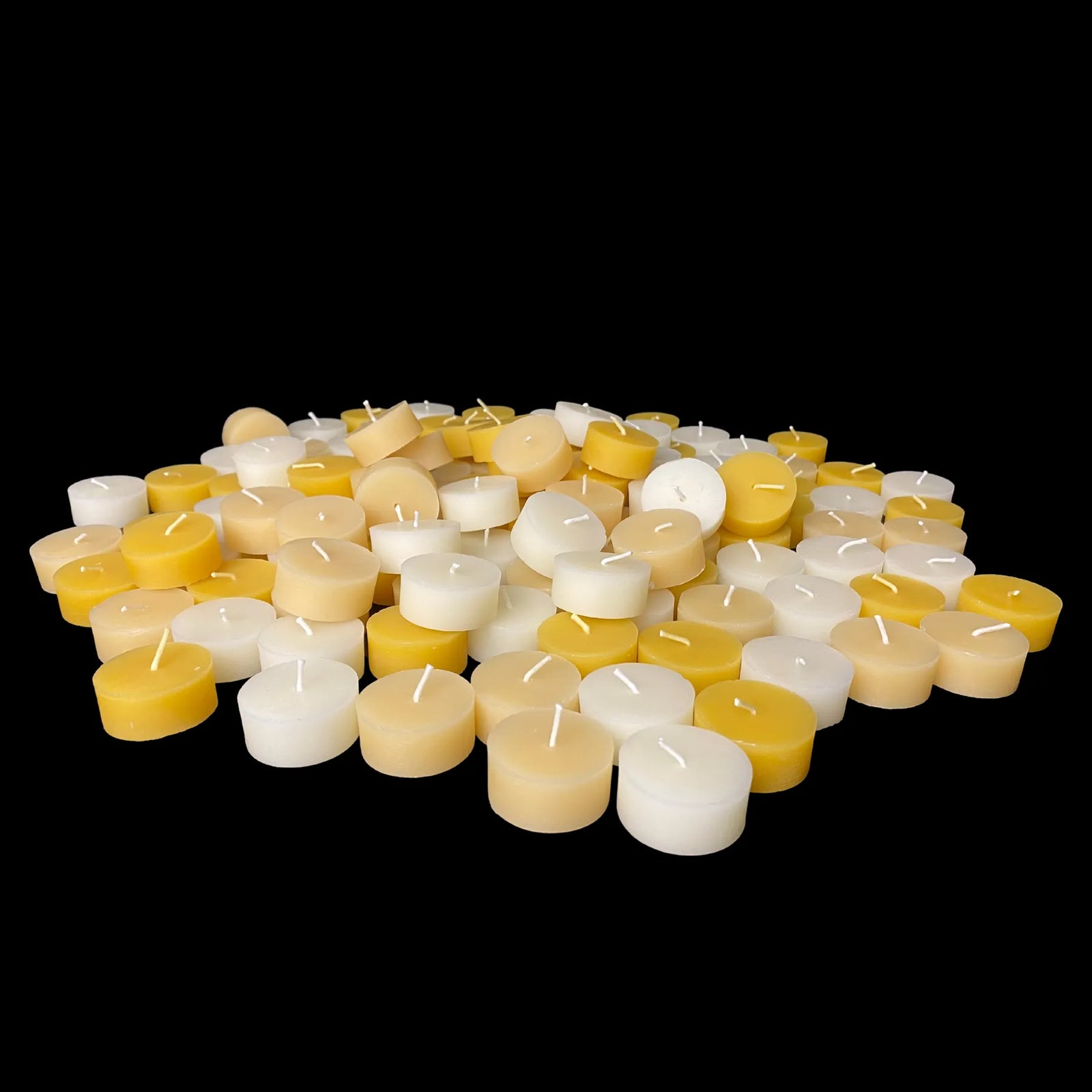 Bulk beeswax tea light refills in white, yellow and cappings spread across black