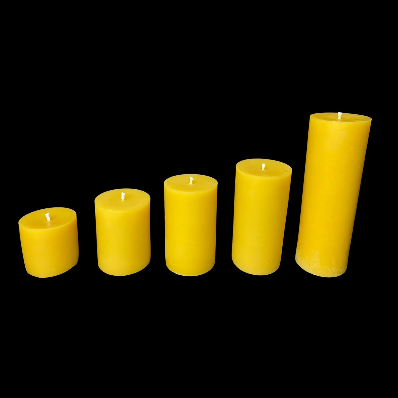 Five 3-inch diameter yellow beeswax pillar candles arranged by size for decor or meditation use.