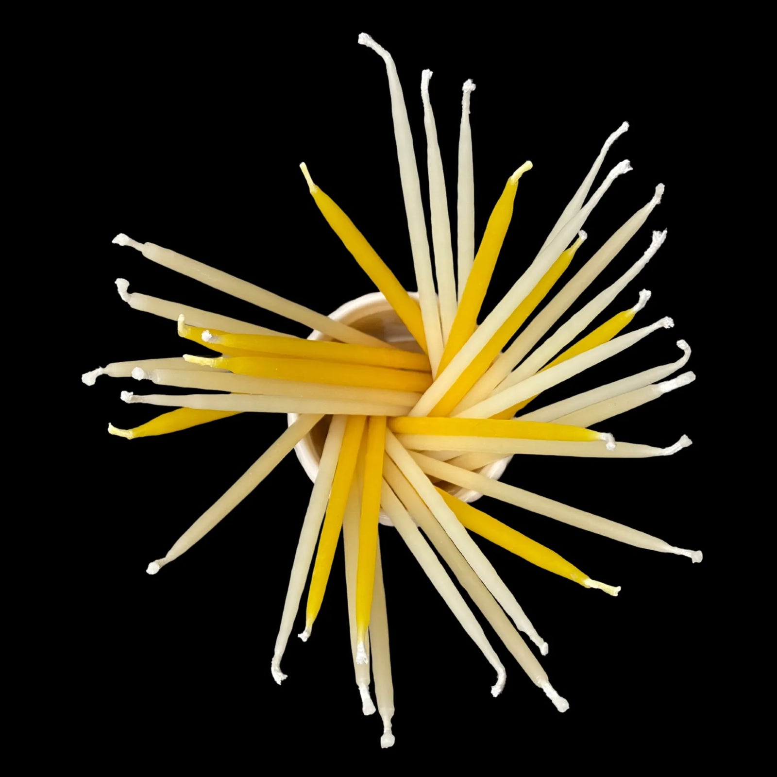 Skinny beeswax birthday taper candles arranged in a starburst with cotton wicks visible